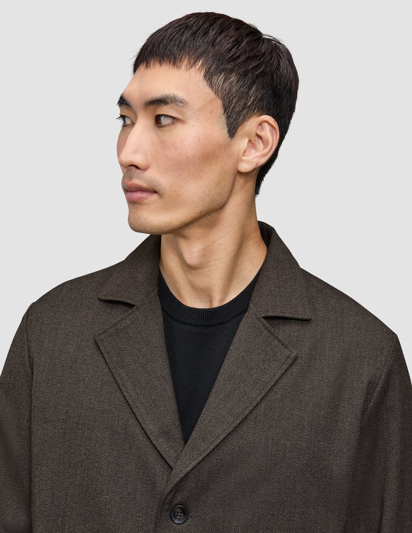 Eine Person, die ein dunkelbraunes Atelier Overshirt mit gekerbtem Kragen über einem schwarzen T-Shirt mit Rundhalsausschnitt trägt.